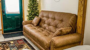 Ein Zimmer mit einem braunen Ledersofa, einem gemusterten Teppich, einem weißen Bett, einer grünen Tür und einem kleinen Weihnachtsbaum.