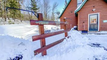 A wooden signpost with directions to restrooms and showers, a wooden building with a green roof, and a snowy landscape.