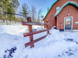 A wooden signpost with directions to restrooms and showers, a wooden building with a green roof, and a snowy landscape. - Trailside Bunkhouse | Sleeps 8 | Ride In, Ride Out (Bessemer Township)