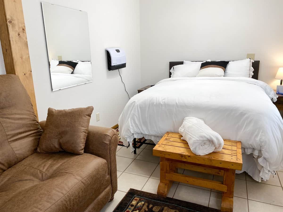 A hotel room with a bed, a wooden bench, a brown sofa, and a wall-mounted air purifier.