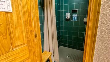 A wooden door with a sign, a shower area with green tiles, a beige curtain, and a small shelf with toiletries.