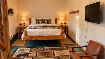 A bedroom with a wooden bed, two bedside tables with lamps, a television on the wall, and a patterned rug.