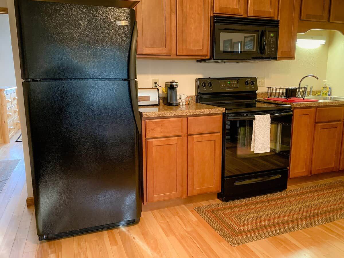 A kitchen with wooden cabinets, a black refrigerator, a microwave, an oven, and a coffee maker.