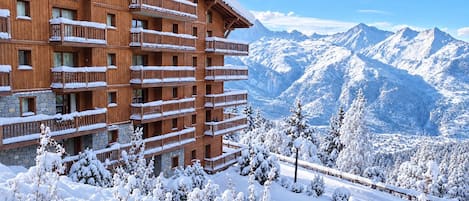 A multi-story wooden building with balconies, surrounded by snow-covered trees and mountains.