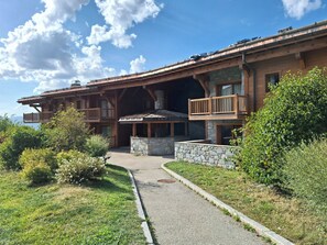 Ein zweistöckiges Holzhaus mit Balkonen, Steinmauern und einem gepflasterten Weg zum Eingang.