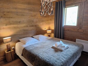 Ein Zimmer mit Holzwänden, einem Bett, zwei Nachttischlampen, einem fenster mit Vorhängen und einer dekorativen Metallleuchte.