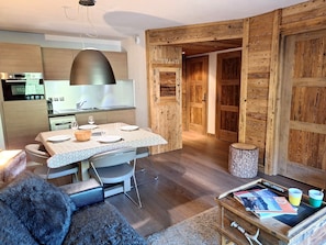 Eine moderne Küche mit Holzausstattung, einem Esstisch für zwei Personen und einer gemütlichen Wohnbereits mit Sofa und Couchtisch.