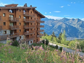 A multi-story wooden building with balconies, set against a backdrop of mountains and a clear sky. - Ski-in/ski-out apartment with Mont Blanc view (Bourg-Saint-Maurice)