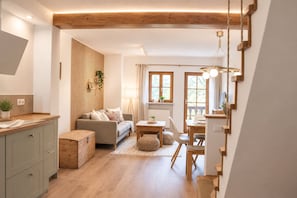 A modern living room with a sofa, dining table, and kitchen area. - Hintergruberhof Vacation Rental (Oberaudorf)