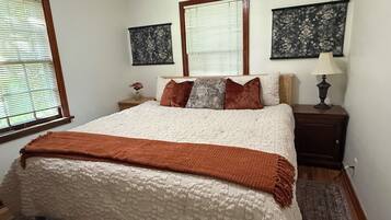 A bedroom with a large bed, two bedside tables, a nightstand, and a window with blinds.