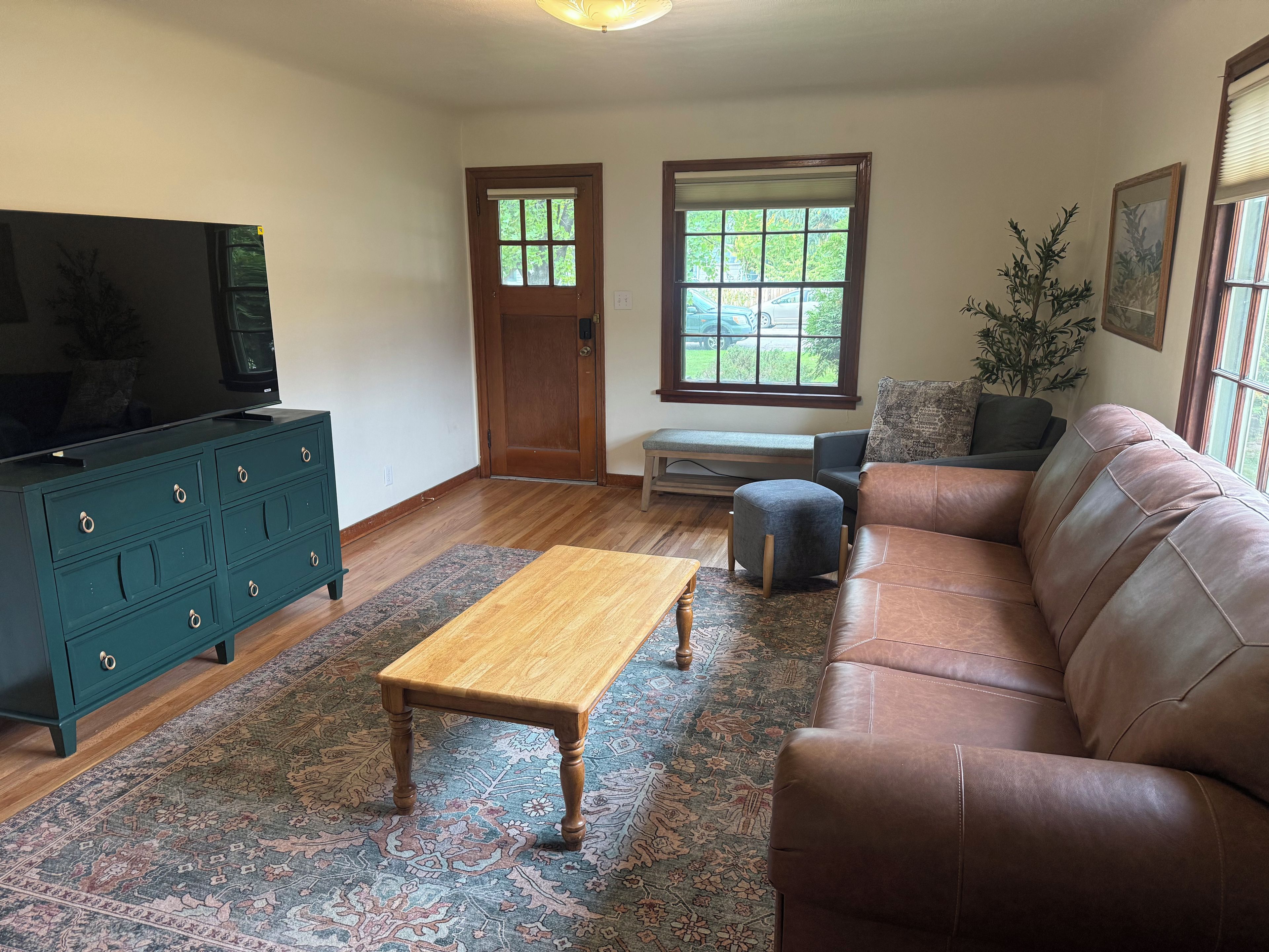 A living room with a wooden coffee table, a brown leather sofa, a green dresser, and a television.