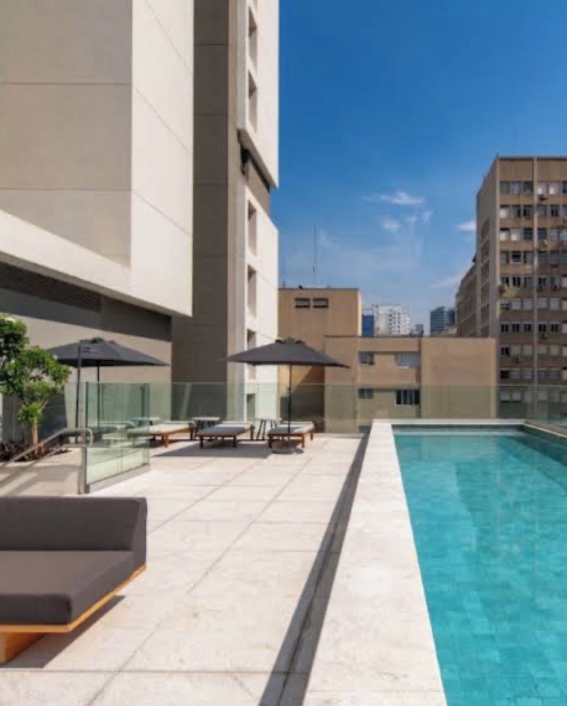 A rooftop pool area with lounge chairs and umbrellas, surrounded by high-rise buildings.