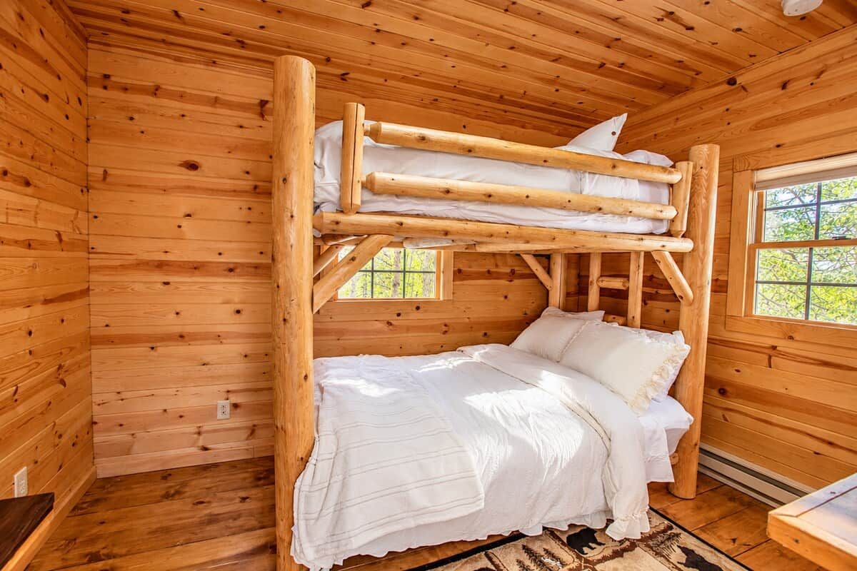 Una cabaña de madera con literas, una ventana con vistas a la vegetación y una pequeña mesa de madera.