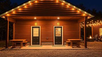 Eine Blockhütte mit zwei Türen, einer Veranda mit Bänken und Lichterketten.