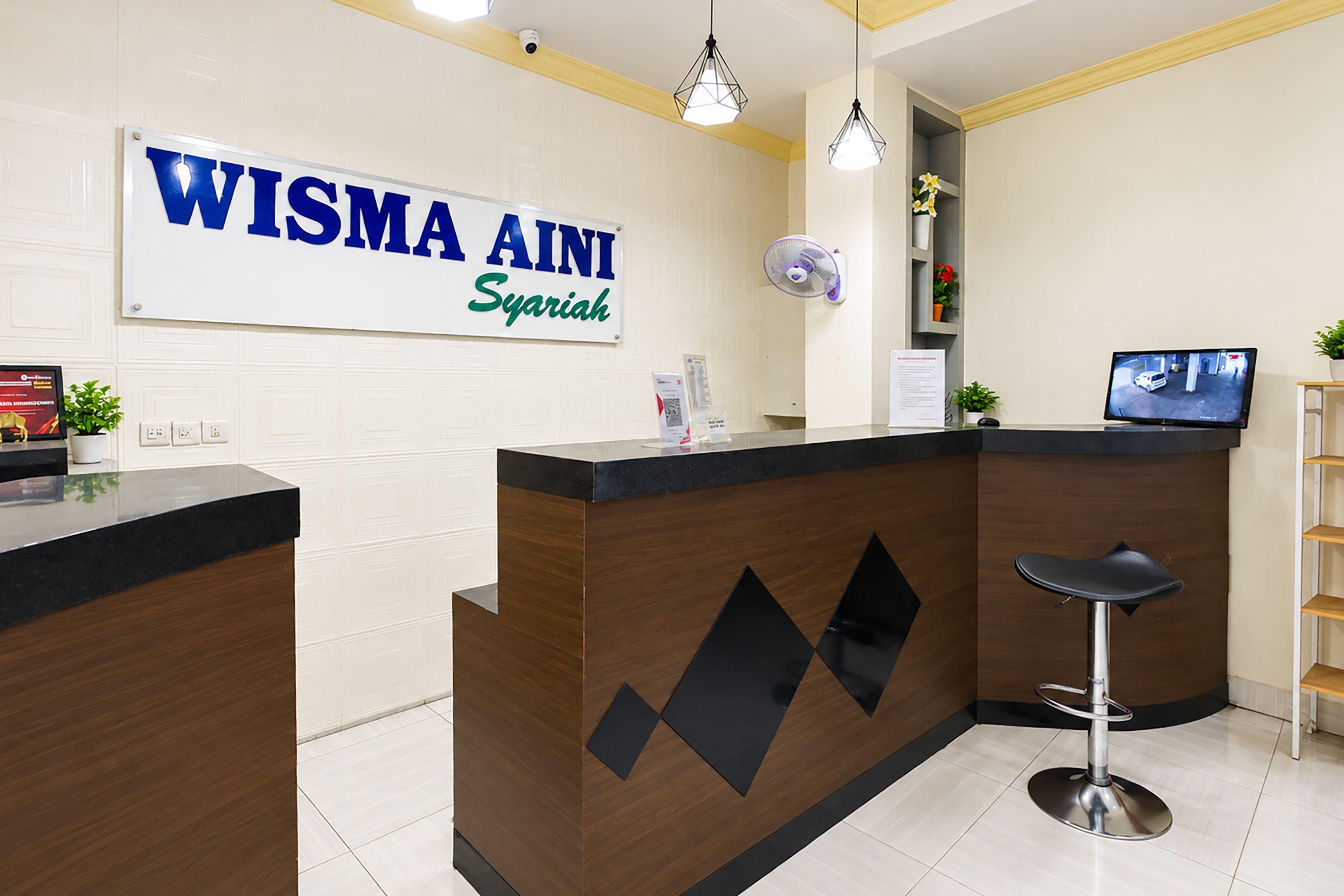 A reception desk with a sign reading 'WISMA AINI Syariah' and a computer monitor on the counter.