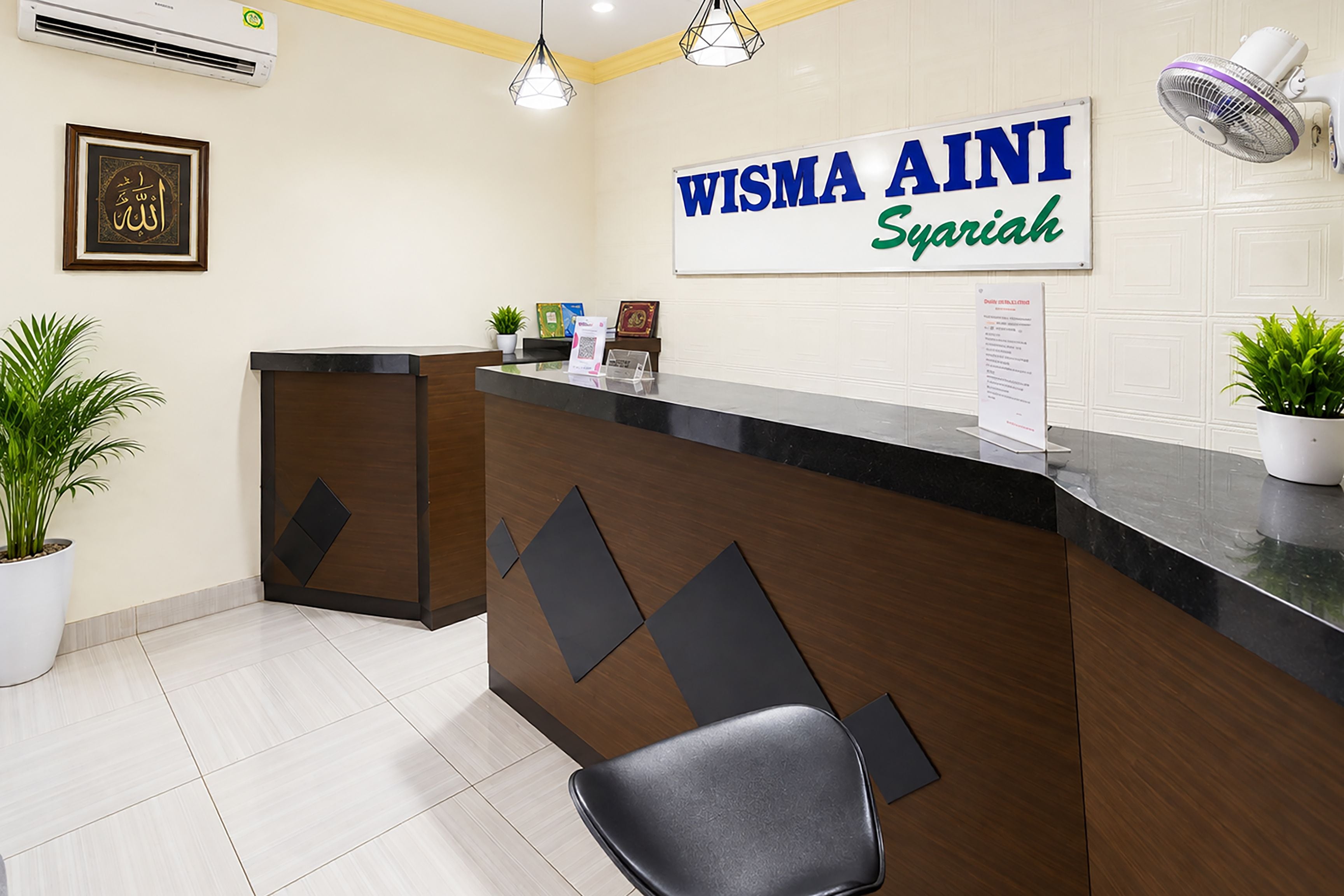 A reception desk with a sign reading 'WISMA AINI Syariah' and a potted plant to the left.