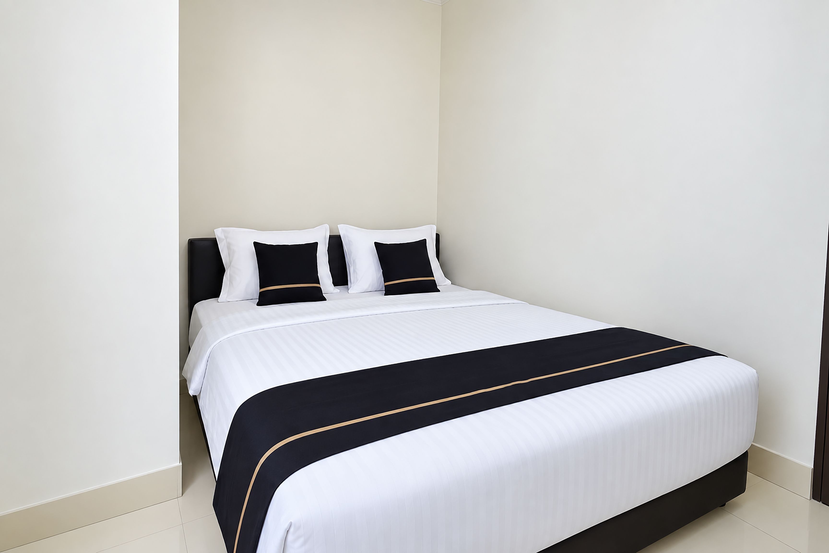 Una cama bien hecha con una colcha blanca y negra, dos almohadas blancas y un cabecero oscuro.