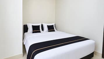 Una cama bien hecha con una colcha blanca y negra, dos almohadas blancas y un cabecero oscuro.