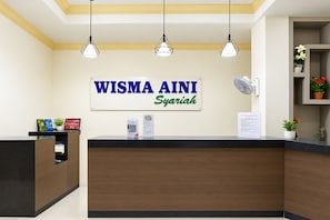 A reception desk with a sign that reads 'WISMA AINI Syariah' and a fan on the wall. - Hotel O near UIN Raden Intan (Bandar Lampung)