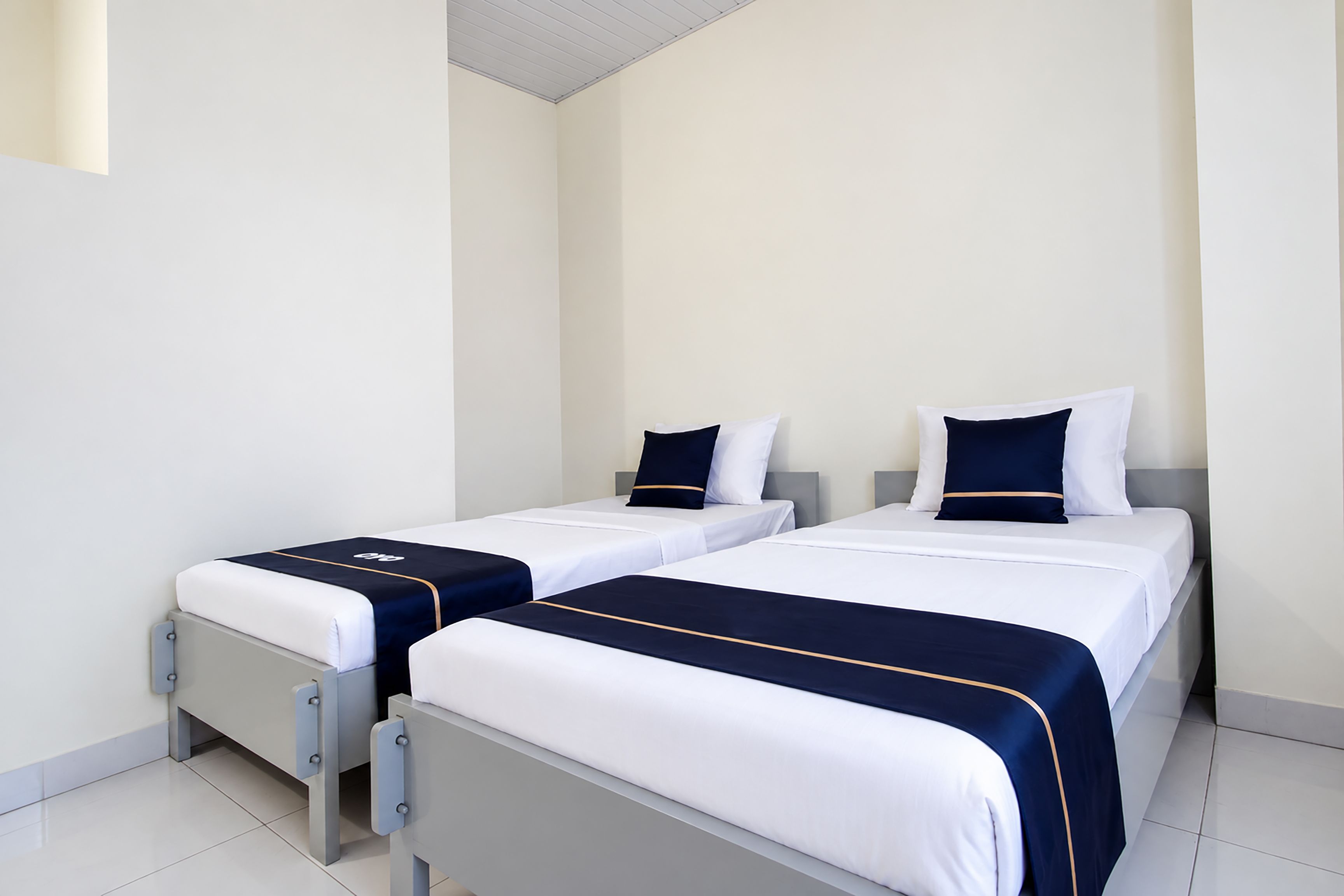 A hotel room with two single beds, each with a white and navy bedspread and matching pillows.