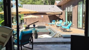 A modern outdoor pool area with lounge chairs and umbrellas, surrounded by a wooden deck and glass doors.