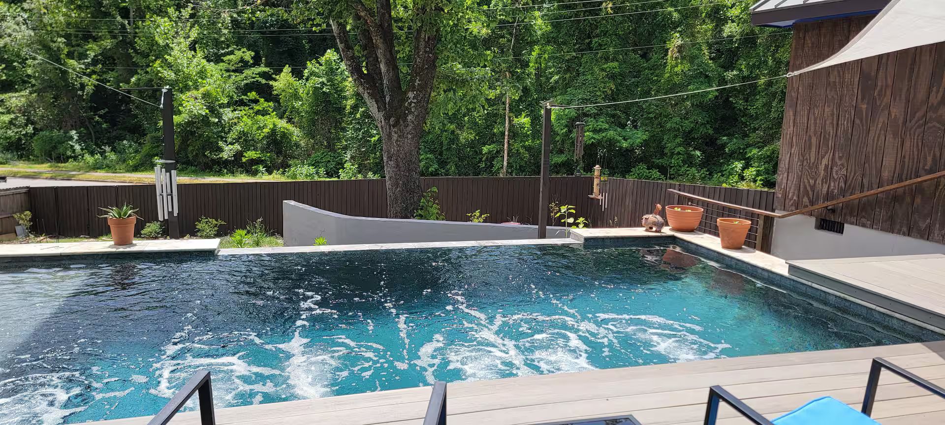 A swimming pool with a wooden deck, surrounded by a wooden fence, and a wooden building in the background.