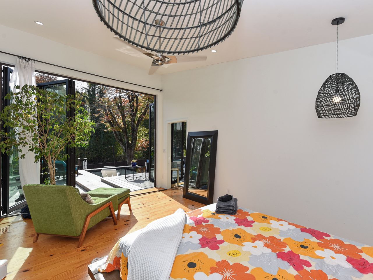 A modern bedroom with a large bed, a green armchair, a ceiling fan, and a view of the outdoors.