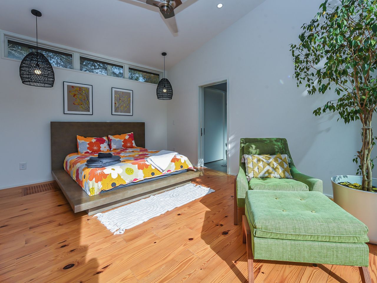 A modern bedroom with a bed, a green armchair, a potted plant, and a ceiling fan.
