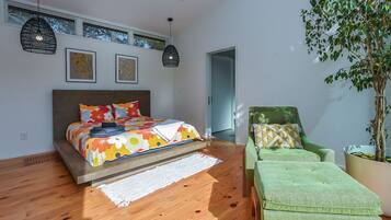 A modern bedroom with a bed, a green armchair, a potted plant, and a ceiling fan.