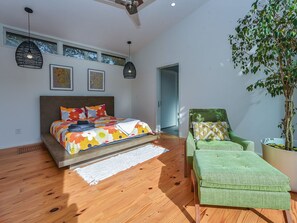 Ein modernes Schlafzimmer mit einem Bett, einem grünen Sessel, einer Topfpflanze und einem Deckenventilator.