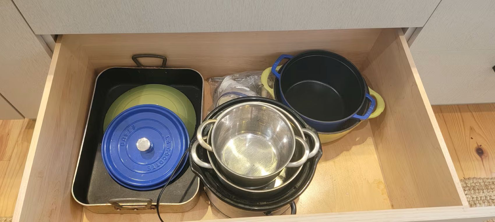 A drawer containing kitchenware including a blue-lidded pot, a green-lidded pot, and a clear pot with a lid.