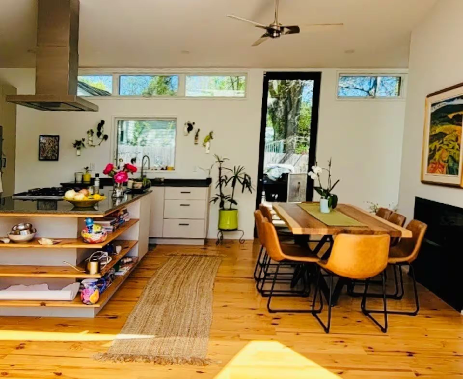 A modern kitchen with a dining area, wooden flooring, and a ceiling fan.