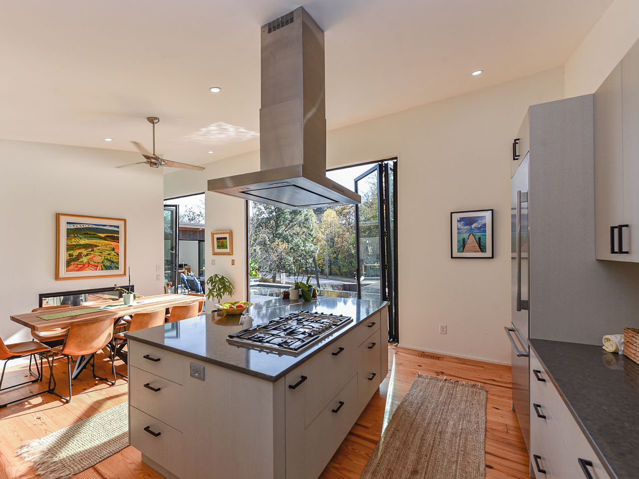A modern kitchen with a central island, a built-in stove, and a large window offering a view of the outdoors.