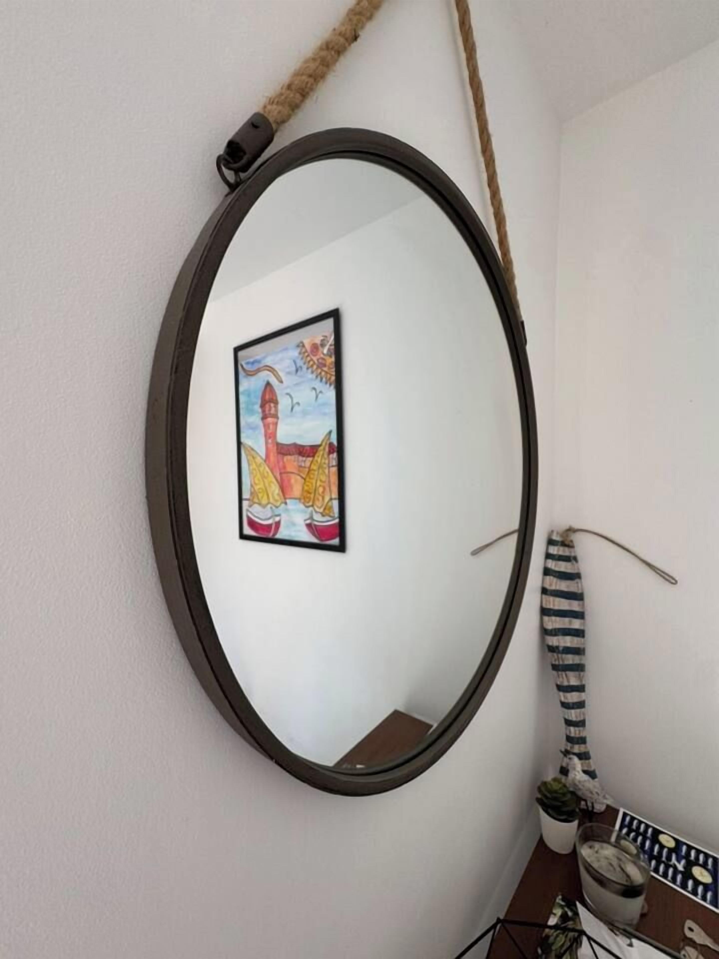 Un miroir rond avec un cadre noir, accroché à un mur blanc, une petite photo encadrée représentant un phare et des voiliers, et un tissu rayé suspendu à proximité.
