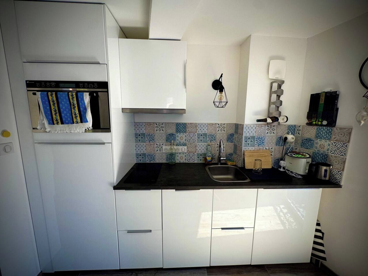 Cocina compacta con armarios blancos, encimera negra y azulejos decorativos.