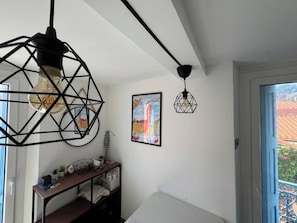 Una habitación con pared blanca, un cuadro colorido enmarcado, una mesita con objetos decorativos y una puerta que da a un espacio exterior.
