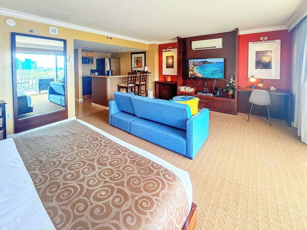 Een hotelkamer met een groot bed, een blauwe bank, een eethoek en uitzicht op de stad.