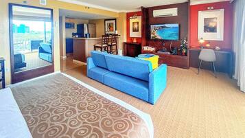 Een hotelkamer met een groot bed, een blauwe bank, een eethoek en uitzicht op de stad.