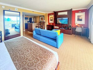 A hotel room with a large bed, a blue sofa, a dining area, and a view of the city. - @ Marbella Lane - Dreamy Oceanview Lanai Waikiki (Honolulu)