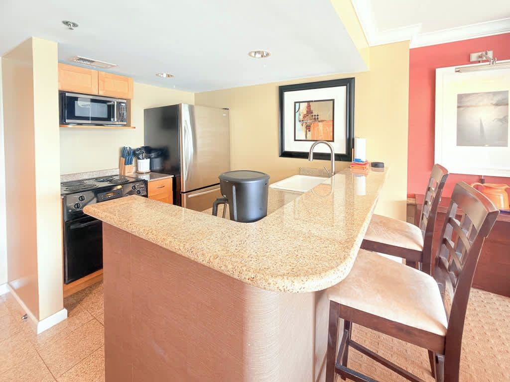 Una cocina con encimera de granito, electrodomésticos de acero inoxidable y una zona de comedor con sillas de madera.