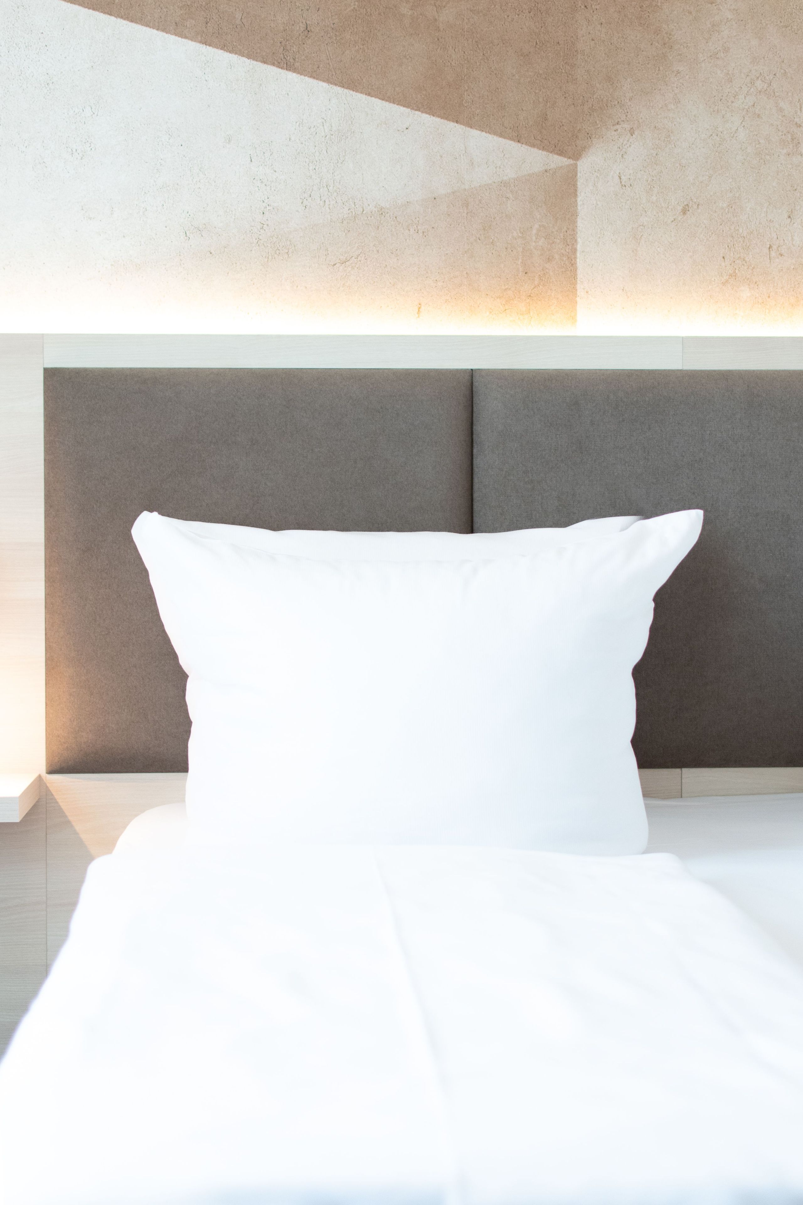 Ein Bett mit einem weißen Kopfkissen und einem Kopfteil mit strukturierter Oberfläche.
