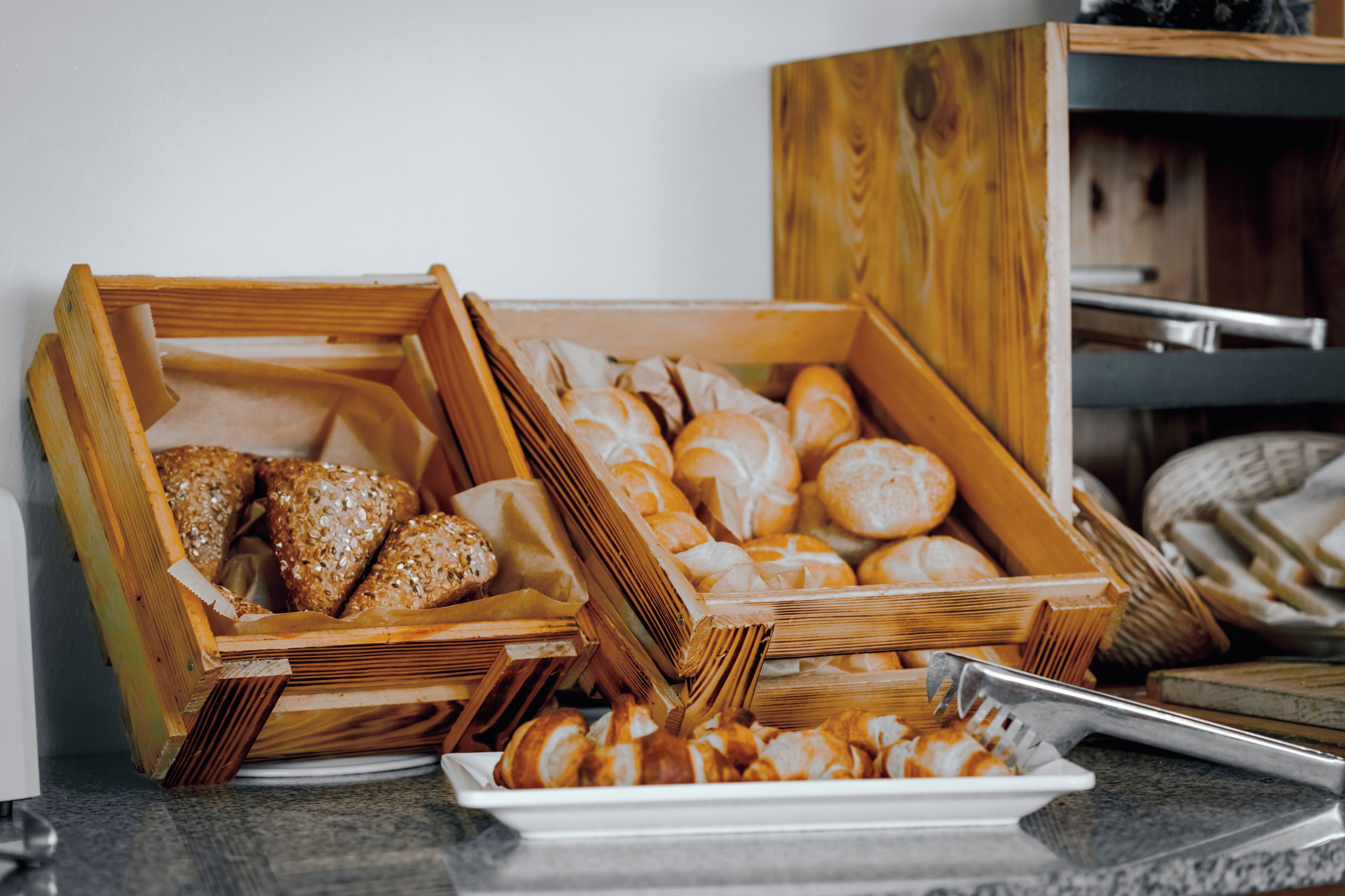 Verschiedene Brotsorten und Gebäckstücke in Holzkästen auf einer Arbeitsplatte.