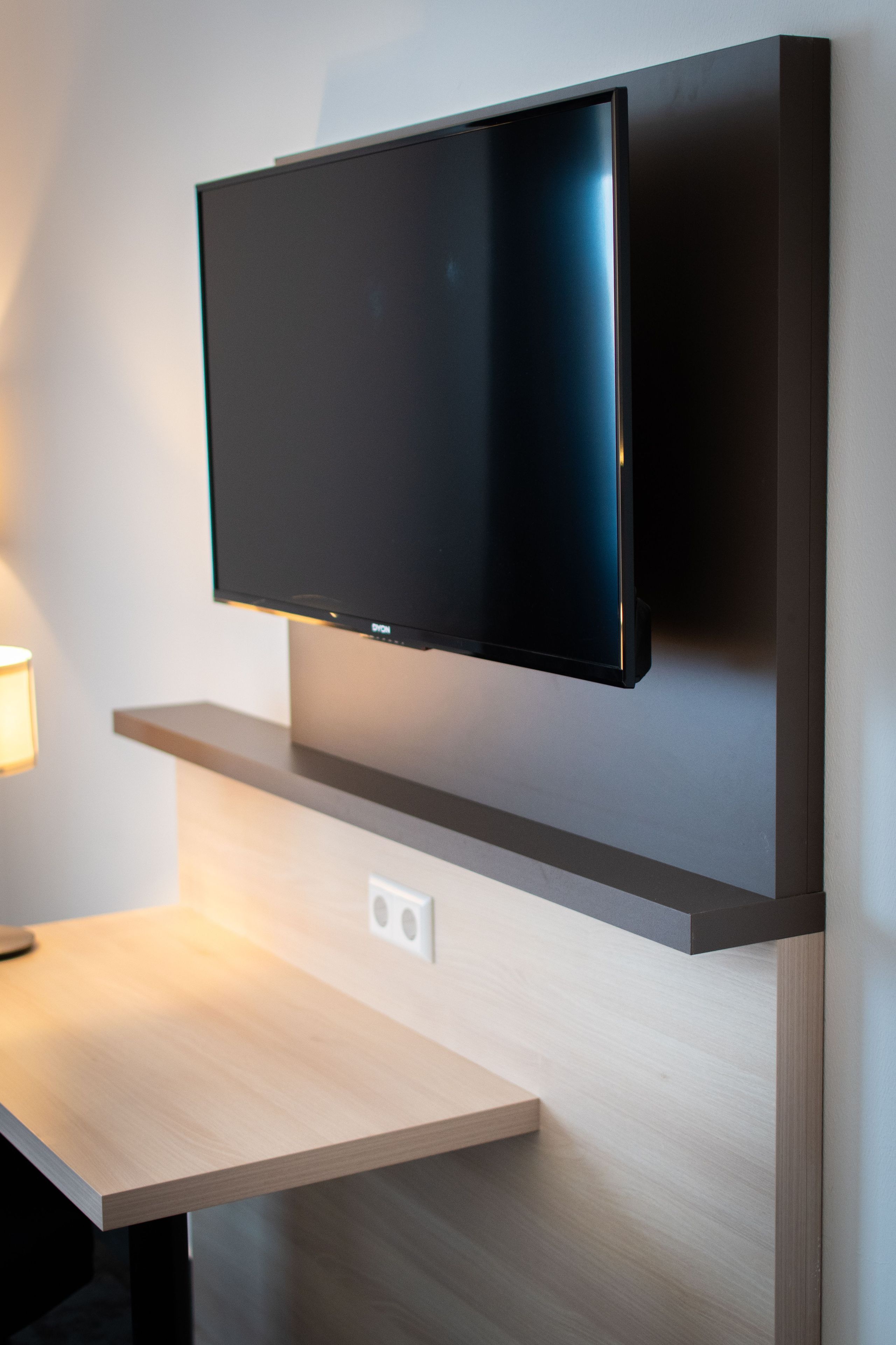 Un téléviseur à écran plat fixé au mur, au-dessus d’une table en bois, avec une source de lumière située à gauche.