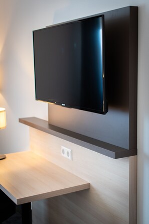 A flat-screen TV mounted on a wall above a wooden table with a light source to the left.