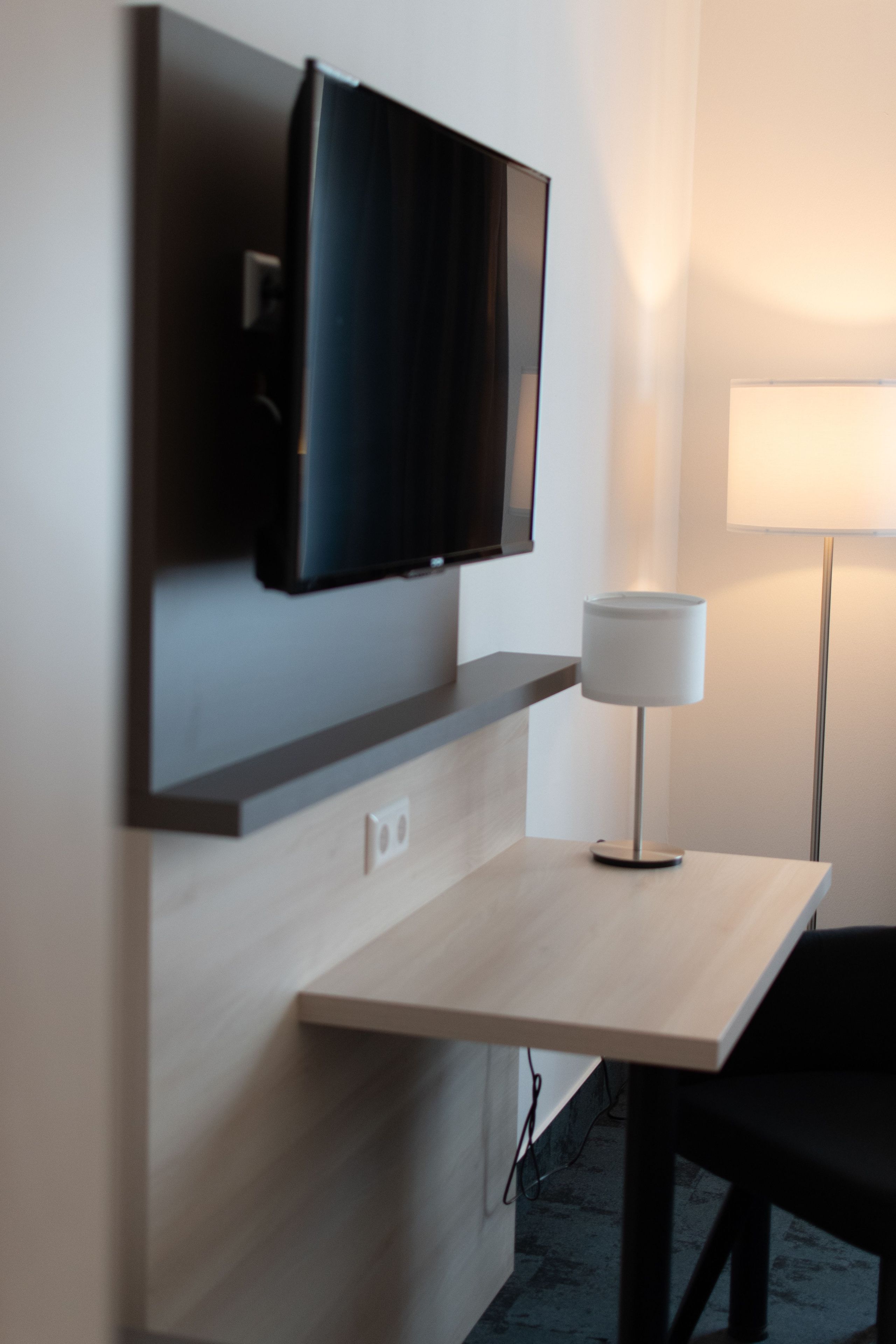 A modern room with a mounted flat-screen TV, a bedside table, and a floor lamp.