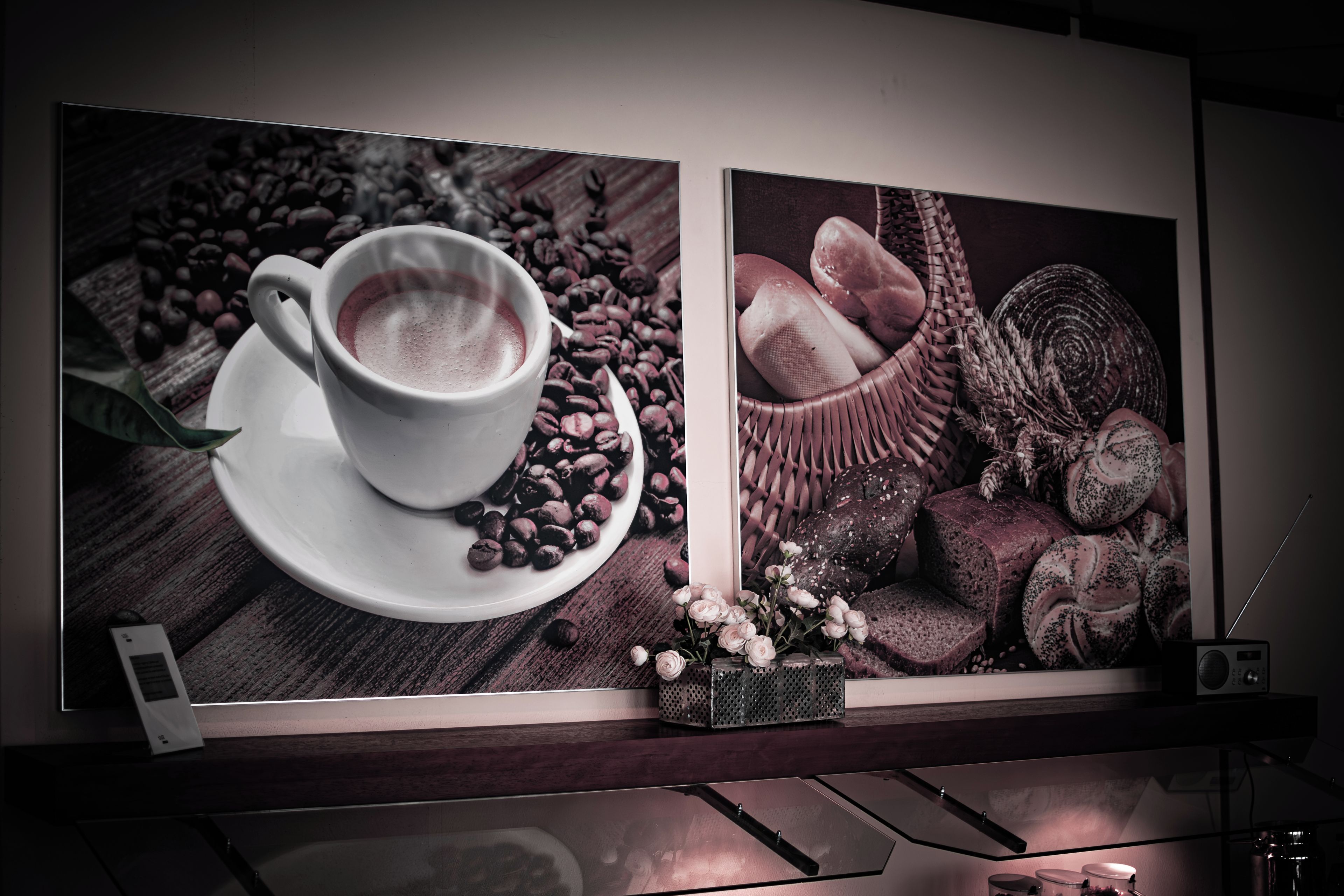 A framed artwork depicting a cup of coffee with coffee beans and pastries on a wooden surface.