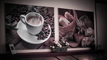 A framed artwork depicting a cup of coffee with coffee beans and pastries on a wooden surface.