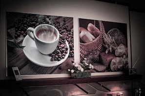 Obra enmarcada que muestra una taza de café junto a granos de café y pasteles sobre una superficie de madera.