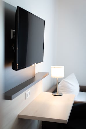 Una habitación de hotel moderna con un televisor de pantalla plana montado, una mesita de noche con lámpara y un enchufe.