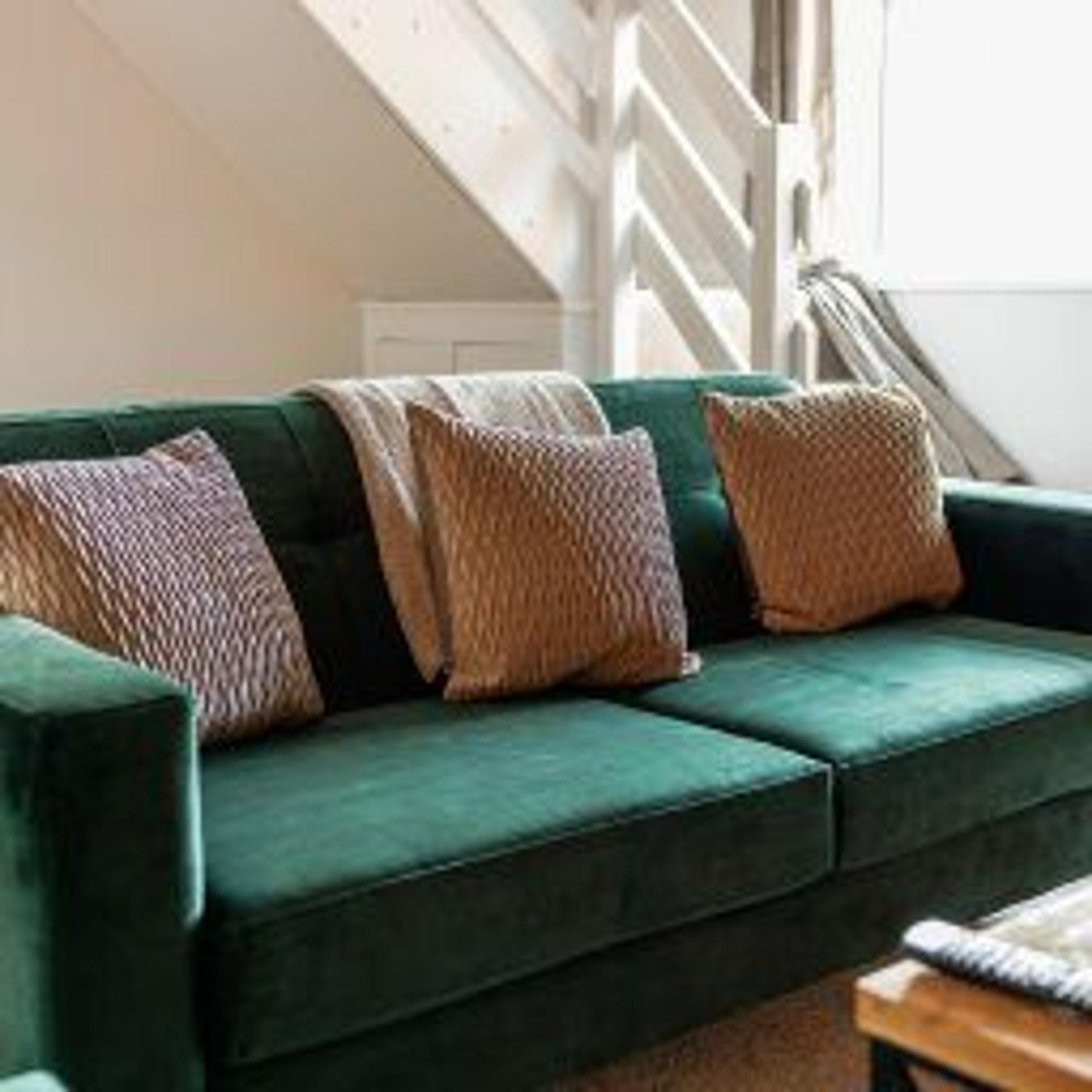 Ein grünes Sofa mit gemusterten Kissen in einem Raum, im Hintergrund eine Treppe.